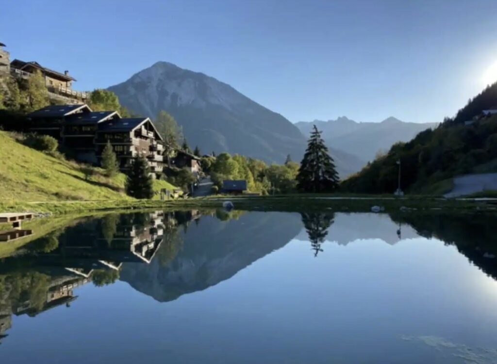 Ein Gewässer in Champagny-en-Vanoise im Sommer, das die Berge und Chalets widerspiegelt.