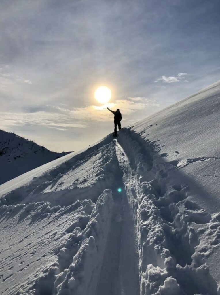 Skitourengeher auf einem schneebedeckten Grat bei Sonnenuntergang in den französischen Alpen.