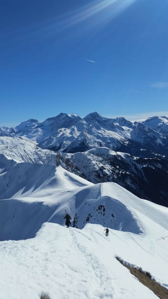 Skitourengeher, die auf einem schneebedeckten Grat mit Panoramablick auf die Savoy Mountains voranschreiten.