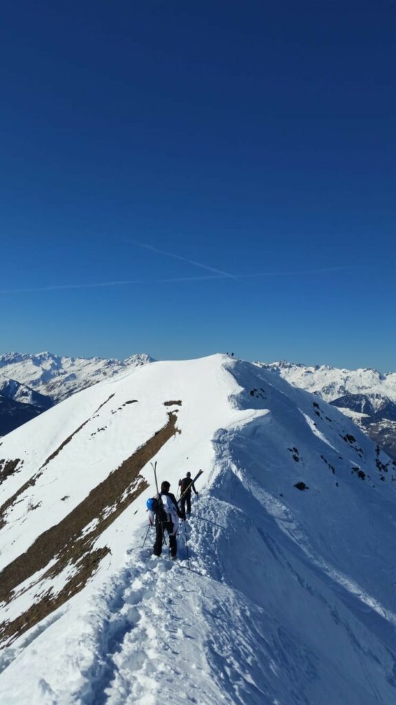 Skitourengeher auf einem verschneiten Hang mit weitem Alpenpanorama